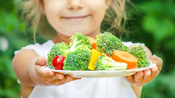 A child holding a plate of fruit and vegetables.