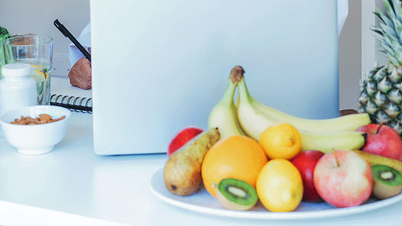 A plate of fruit in the foreground and person working at a laptop in the background.