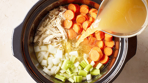 Chicken, carrots and leeks in a slow cooker and a person adding stock from a jug.
