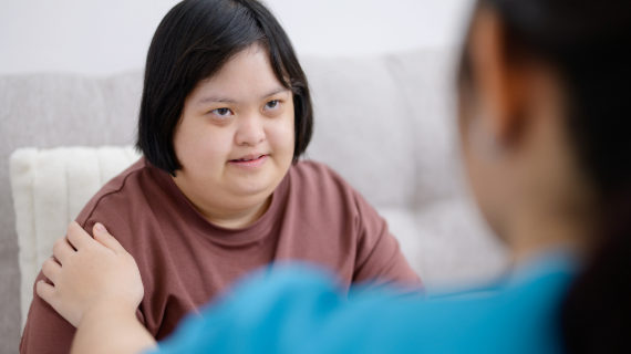 A nurse In blue uniform placing her hand on the should of a lady with learning disability.
