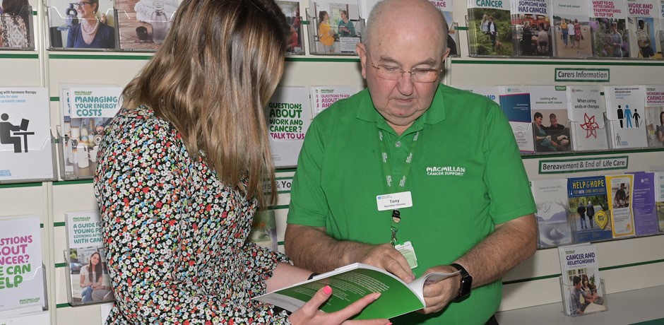 A volunteer wearing a Macmillan Cancer Support t-shirt shows an information leaflet to a woman standing beside him.