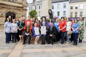 A large group of people outside Coleraine Town Hall. The group is made up of Council and Health and Social Care representatives. Some are wearing uniforms and robes.