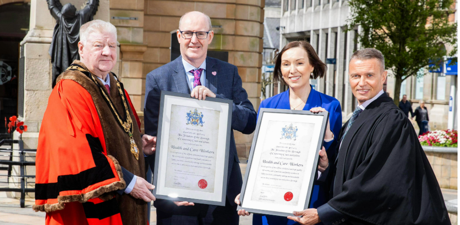 The Mayor of Causeway Coast and Glens Borough Council wearing red robes, with Health Trust Chief Executives holding framed certificates along with the Council Chief Executive wearing black robes