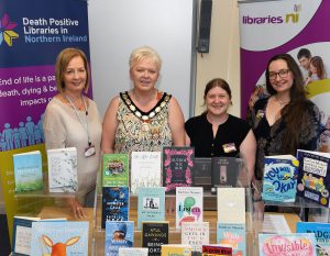Three ladies standing in front of a table. There are books on display on the table and pop-up banners in the background