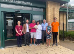 Seven people standing outside Antrim Laboratory. One is holding an award