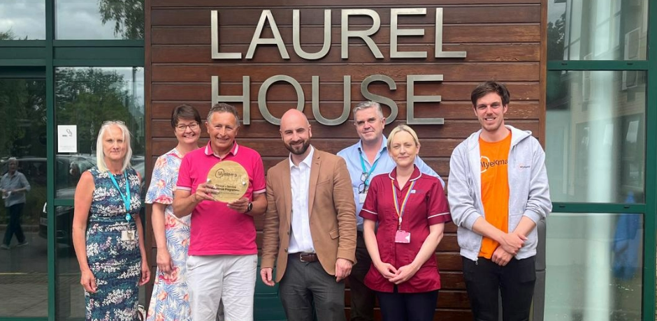 A group of seven people standing outside Laurel House. One person is holding an award.