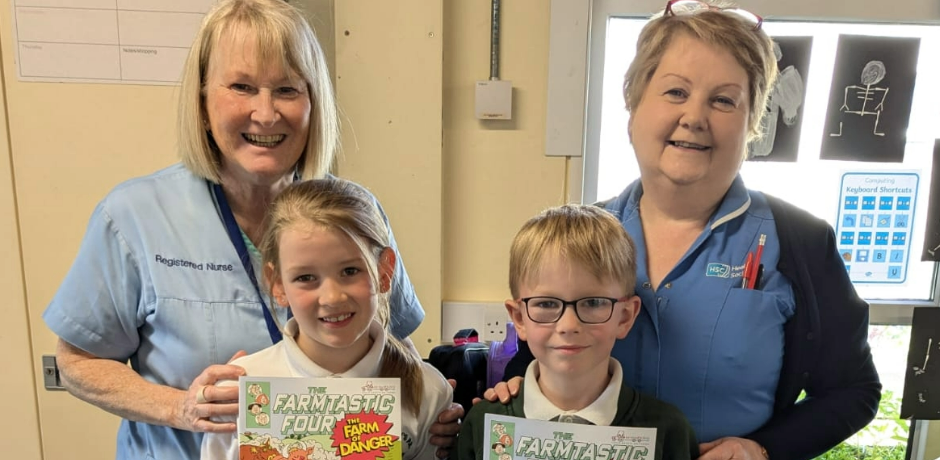 Two members of staff stand beside two children holding Farm Safety comics