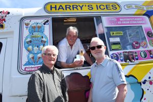 A man lean out of an ice-cream van window, with two customers standing beside the van