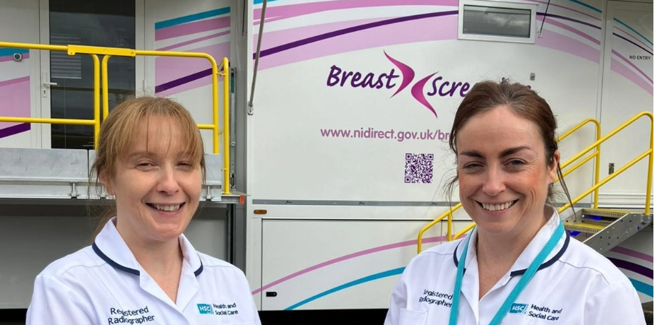 Two members of staff in uniform standing in front of a mobile breastscreening unit.
