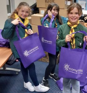 Three girl scouts holding purple encompass branded bags