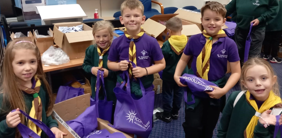 A group of scouts standing together holding purple bags with boxes visible in the background
