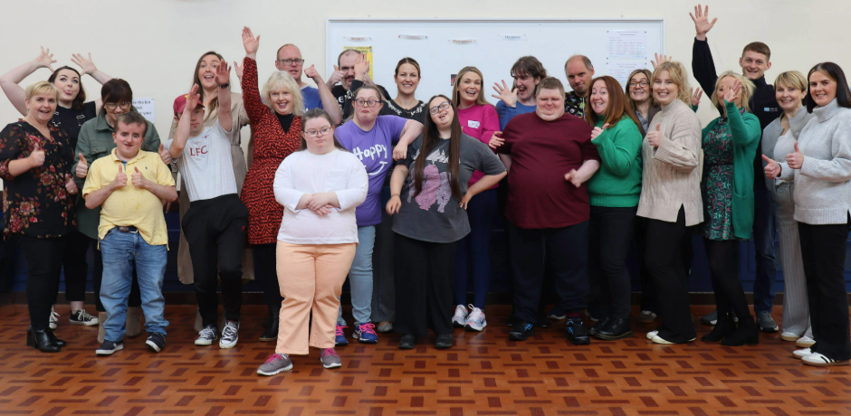 A large group of people standing together looking happy, Some are putting their thumbs up and others are waving