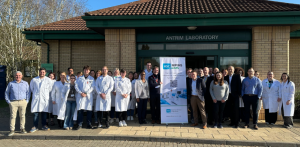 A large group of people standing outside Antrim Laboratory. There is a pop-up stand in the middle of the group, and some people are wearing white coats