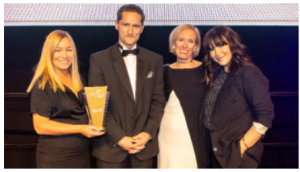 3 females and 1 male in formal attire accepting an award