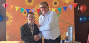 Two men stand beside each other, they are shaking hands.