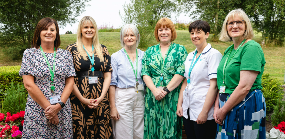 Six women standing beside each other in a garden setting