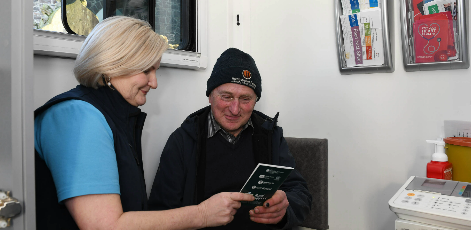 A farmer looks at an information leaflet while sitting beside a member of the Farm Families team.