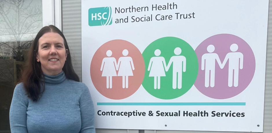 Dr Sharon Porter standing outside a building, beside a sign for Contraceptive and Sexual Health Services.