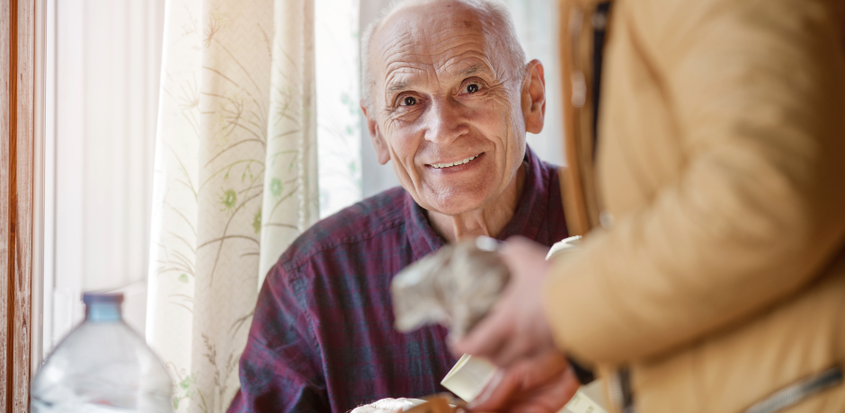 A smiling elderly man, with an other person visible beside him