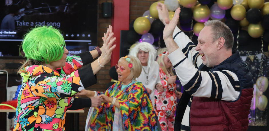 A woman in 70's themed fancy dress dances with a service user