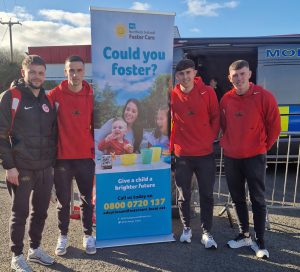 Football players stand beside a pop-up banner about fostering.