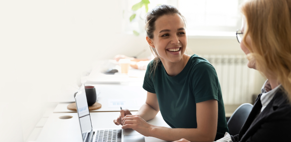 Two women sit together with a laptop in front of them