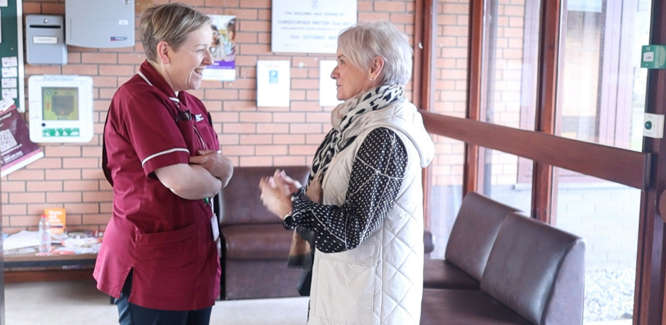 A nurse and a woman standing in a foyer area, talking to each other