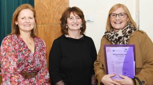 Three women standing beside each other, one is holding a purple folder.