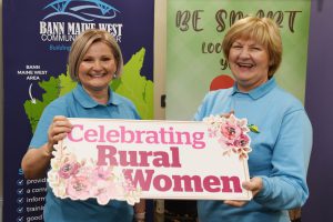 Two women standing front of pop-up stands. They are holding a sign which reads 'celebrating rural women'.