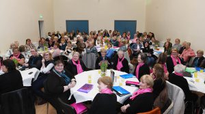 Women sitting around circular tables in a large room.