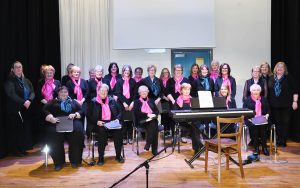 Choir members wearing black shirts and pink scarves.