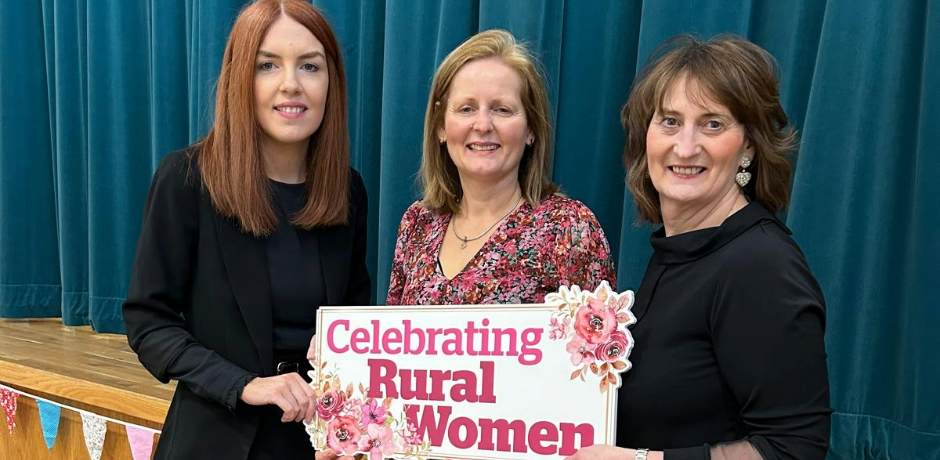Three women standing together holding a sign which says 'celebrating rural women'