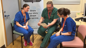 Three doctors, one male and two female, in conversation about the contents of a booklet the male doctor is holding