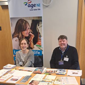 Two people sitting behind a table with pop-up stands behind. Leaflets are on the table.