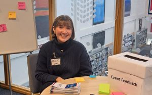 A woman sitting at a table. There is a box on the table with 'event feedback' written on the side.