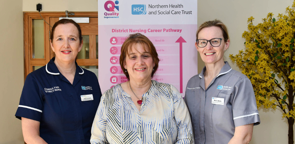 Three women, two in nursing uniform, standing in front of a pop up banner that says District Nursing Career Pathway
