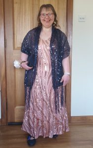 A woman wearing a full length evening dress smiles as she stands in front of a door.