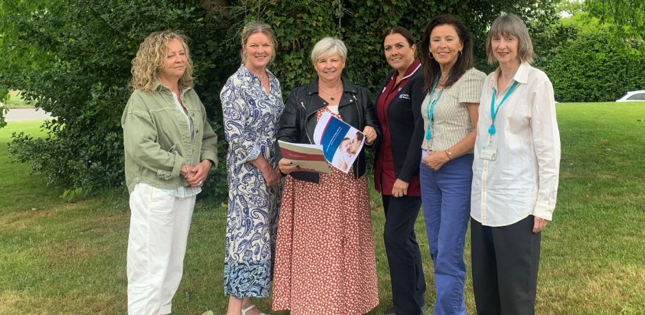 Six women standing together outside. One lady is holding a booklet.