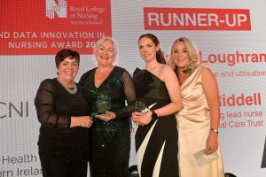 Rita Devlin stands to the left wearing a black dress with Maria Loughran and Caroline Riddell who are each holding a glass trophy, with Claire Buchner stands to the right.