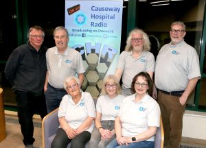 A group of people standing and sitting beside a banner about Causeway Hospital Radio.