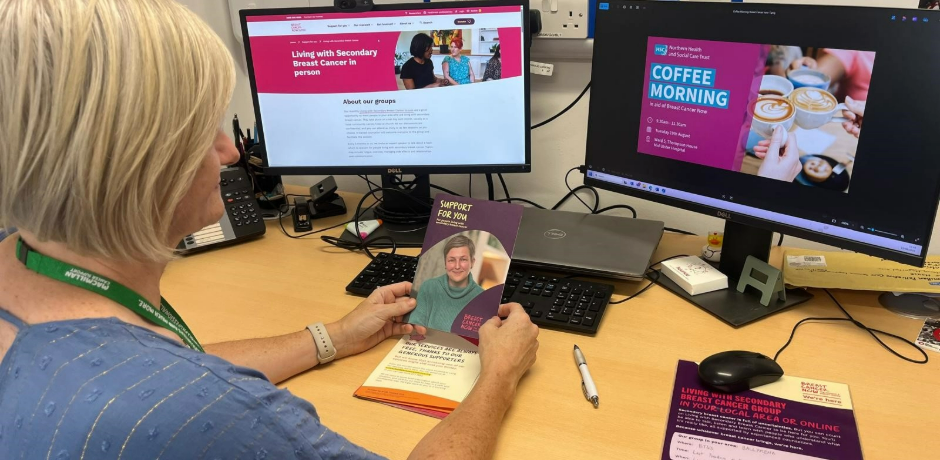 A woman sits at a desk with two computer screens in front of her. She is looking at information about Breast Cancer Now