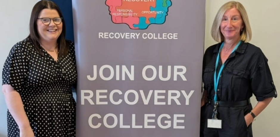 Two women stand beside a pop-up about banner with text on it which reads 'join our recovery college'