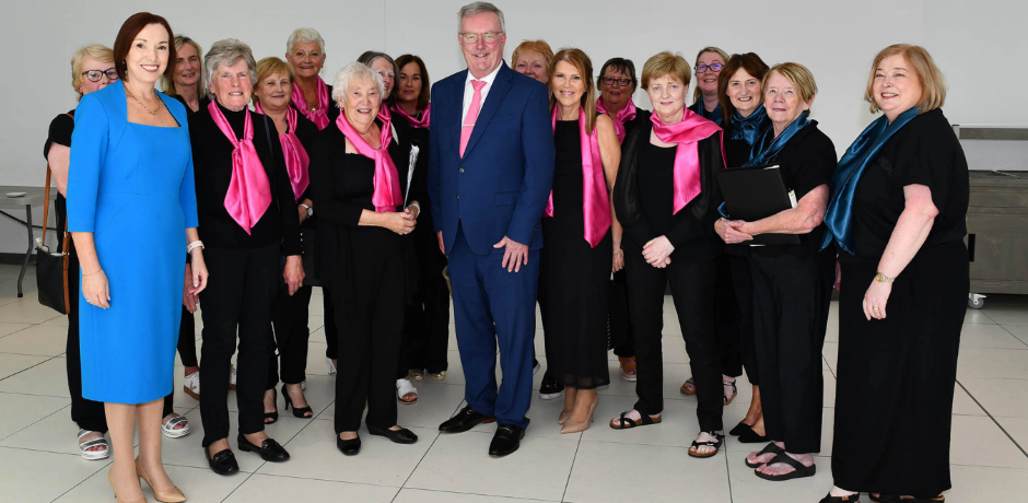 Members of the Rural Melody Ladies Choir, dressed in black with pink scarves, with Northern Trust Chief Executive Jennifer Welsh and Health Minister Mike Nesbitt.