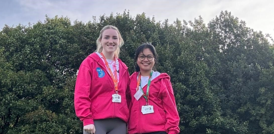 Hazelle Ongcoy and Caillee McHugh standing together outside. They are wearing matching pink jumpers and there are trees behind them.