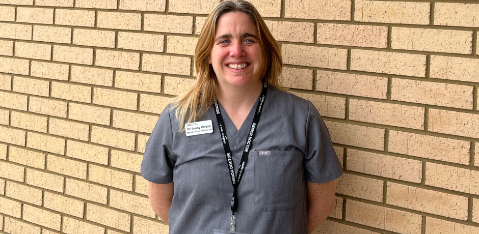Dr Jennifer Wilson wearing a grey uniform standing against a brick wall.
