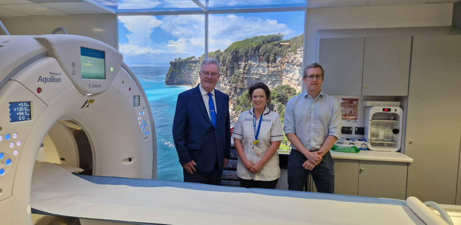 Three people standing beside a scanning machine.