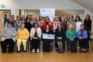 A large group of women sitting and standing together. One is holding a sign which reads 'singing for fun'.