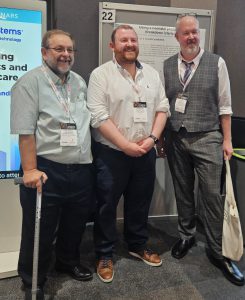 Three men stand in front of a poster display.