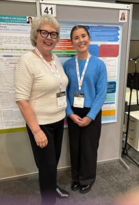 Two women stand in front of a poster display