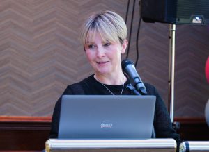 A woman speaks with a microphone and laptop in front of her.